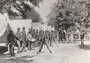 Men in military uniforms stand outside their tents on camp ground