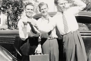 Photograph of three young men standing beside car